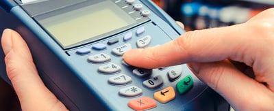 A finger pushes a button on a credit card payment terminal