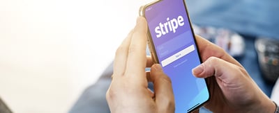Hands holding a smartphone that displays the login page for the Stripe app